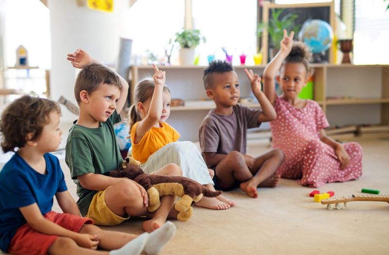 group-small-nursery-school-children-sitting-floor-indoors-classroom-raising-hands-1024x671 (1)